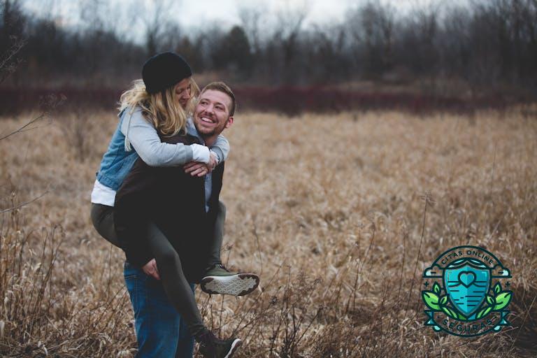 A happy couple enjoys a playful moment in a field during the day, symbolizing love and joy.